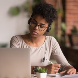 Focused mixed race woman wearing headphones watching webinar write notes