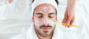 Portrait of man with clay facial mask in beauty spa.