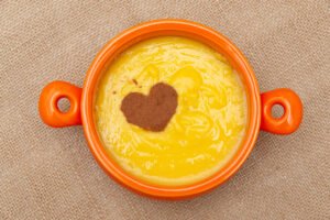 Homemade sweet corn pudding known in Brazil as Curau or Canjica Nordestina in ceramic bowl. Powdered cinnamon in the heart shape. Isolated on jute background. Close-up. Top view